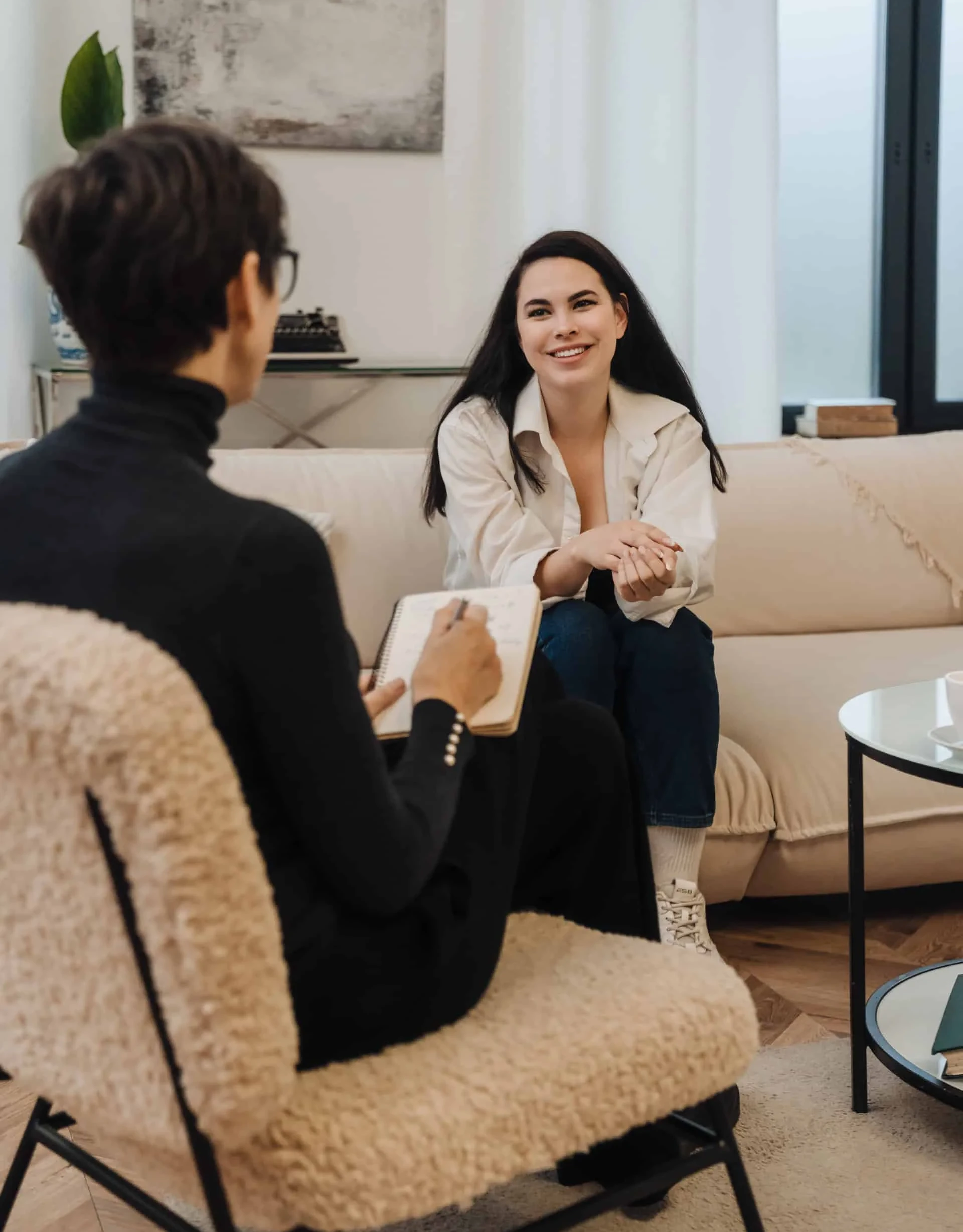 Psychologist writing down notes during therapy session with smiling woman